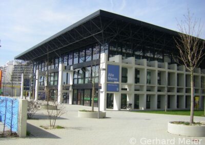 Ein modernes Gebäude mit markanter Stahl-Glas-Dachkonstruktion und geometrischer Fassade aus Beton kombiniert innovatives Design mit funktionaler Architektur.