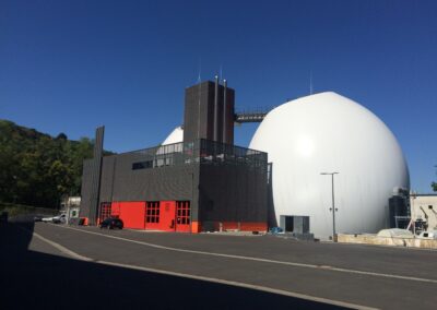 Ein modernes Industriegebäude mit roten Eingangstoren, dunkler Fassade und einer auffälligen weißen Kugel daneben unter klarem Himmel.