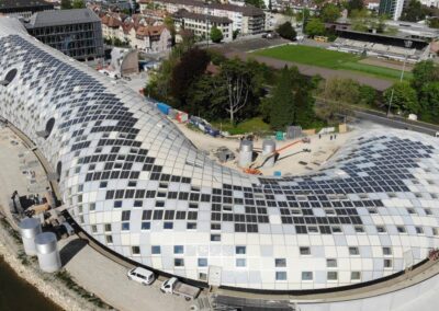 Ein modernes, futuristisches Gebäude mit charakteristischer weißer Fassade und regelmäßig angeordneten dunklen Fensterquadraten liegt an einem Fluss in einer europäischen Stadt.
