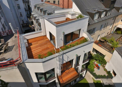 Moderne weiße Wohngebäude mit Holzterrassen und begrünten Dächern in dichter urbaner Bebauung.