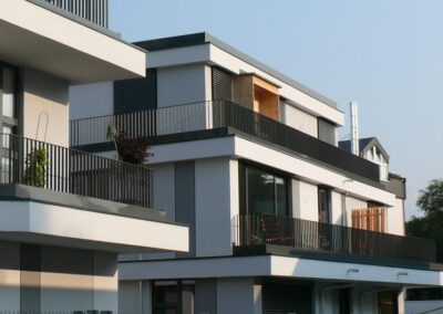 Ein modernes, mehrstöckiges Wohngebäude mit weißer Fassade, schwarzen Metallbalkonen und großflächigen Fenstern in zeitgenössischer Architektur.