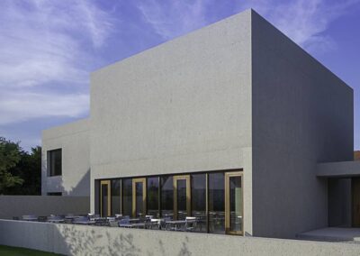 Ein modernes Betongebäude mit geometrischen Formen, großflächigen Fenstern und einer minimalistischen Architektur unter blauem Himmel.