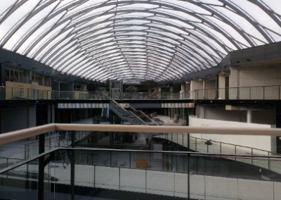 Ein modernes Gebäudeinneres mit gewölbter Glaskonstruktion, mehreren Etagen und minimalistischer Architektur in Grau und Weiß.