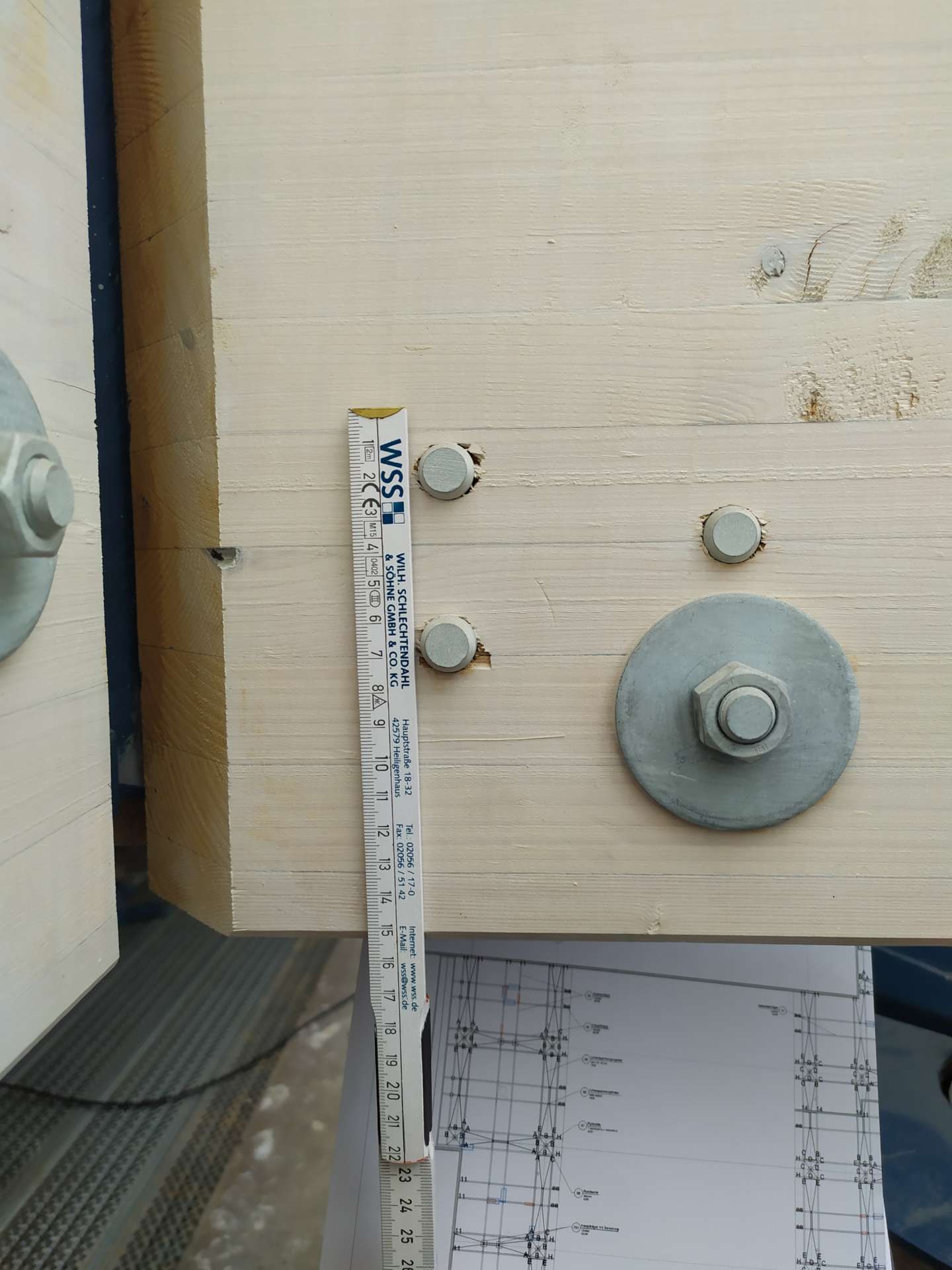 Ein Holzbrett mit metallischen Befestigungselementen und einer Messskala zeigt architektonische Konstruktionsdetails.