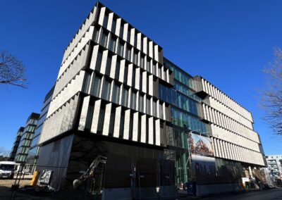 Ein modernes Gebäude mit markanter weißer Betonarchitektur und charakteristischen vertikalen Lamellenelementen an der Fassade unter blauem Himmel.