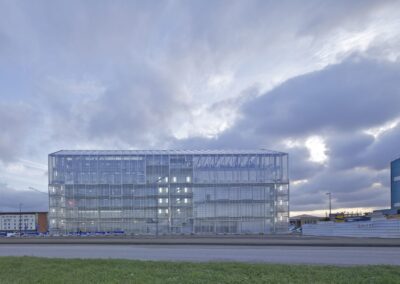 Ein modernes Glasgebäude mit transparenter Gitterfassade steht am Flughafen unter bewölktem Himmel.