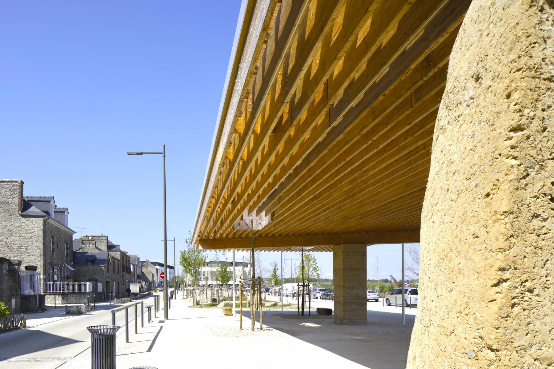 Ein moderner Betonviadukt mit gelber Unterseite überspan­nt eine gepflasterte Promenade neben historischen Steingebäuden.