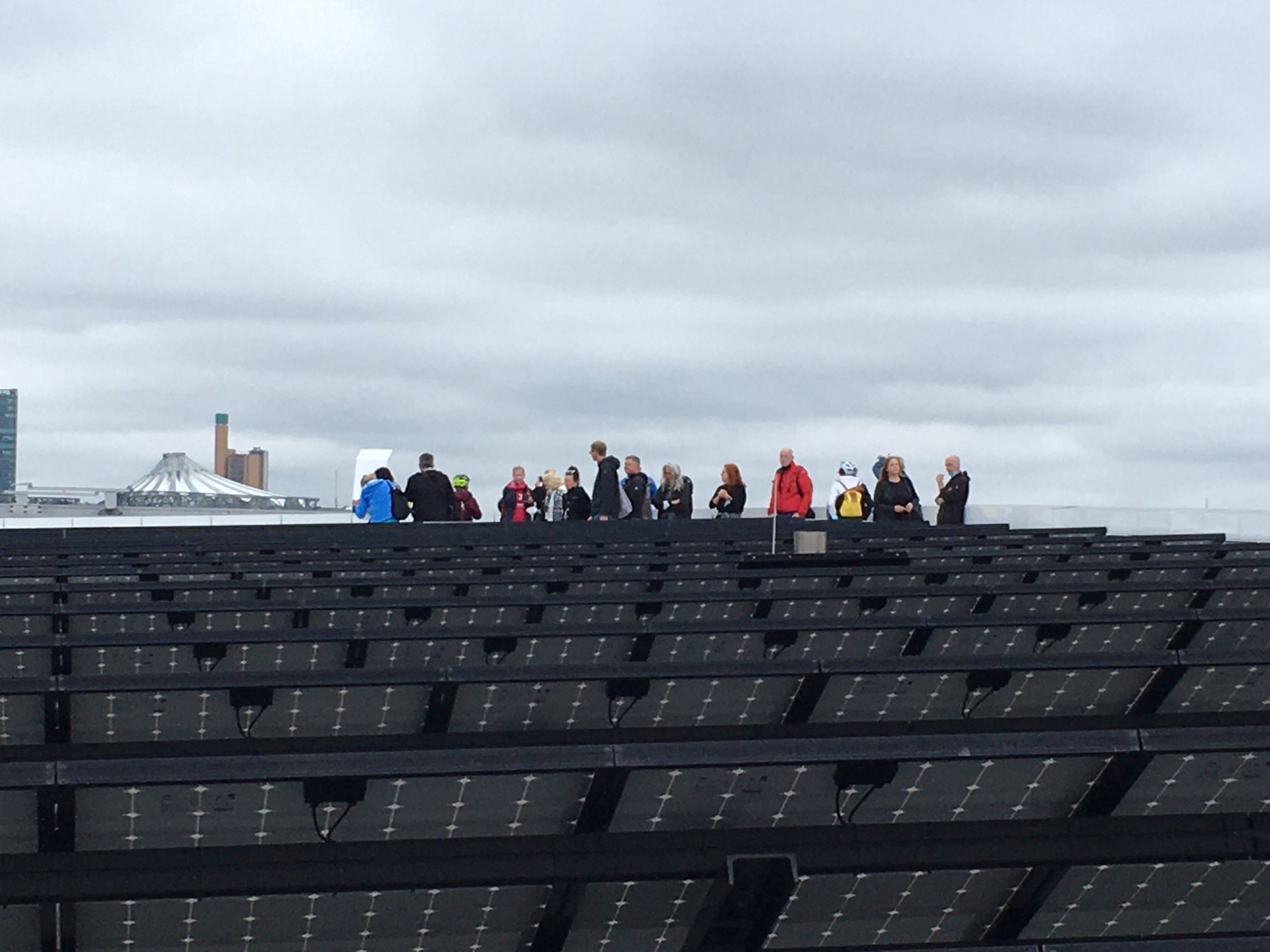 Eine Gruppe von Menschen steht auf der Dachkante eines modernen Gebäudes mit charakteristischer schwarzer Solaranlage-Fassade.