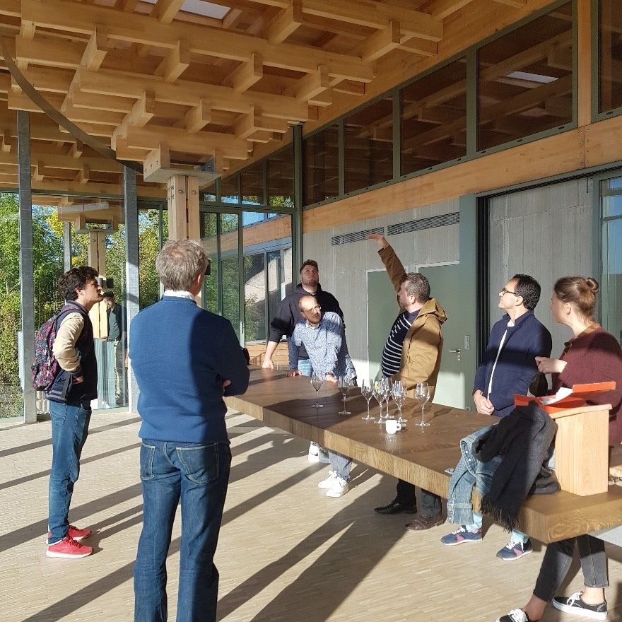 Eine Gruppe von Menschen steht in einem modernen Holzgebäude mit kassettierter Decke, großen Glasfassaden und minimalistischem Design.
