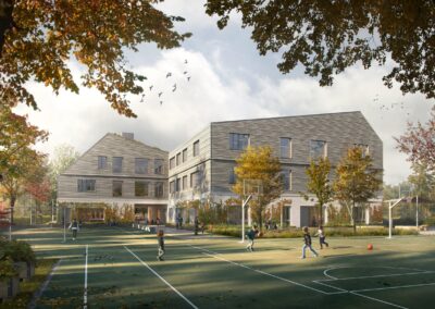 Ein modernes Schulgebäude mit grauer Metallverkleidung und Satteldächern liegt in herbstlicher Parklandschaft mit Sportplatz.