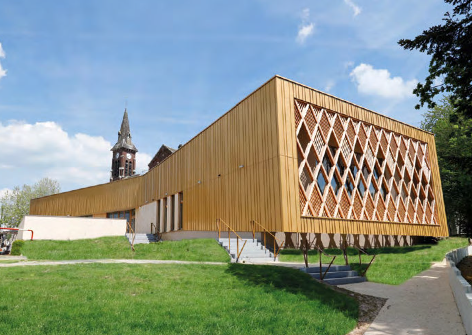 Ein modernes Gebäude mit goldener Metallverkleidung und geometrischem Muster steht neben einer historischen Kirche mit Turm.