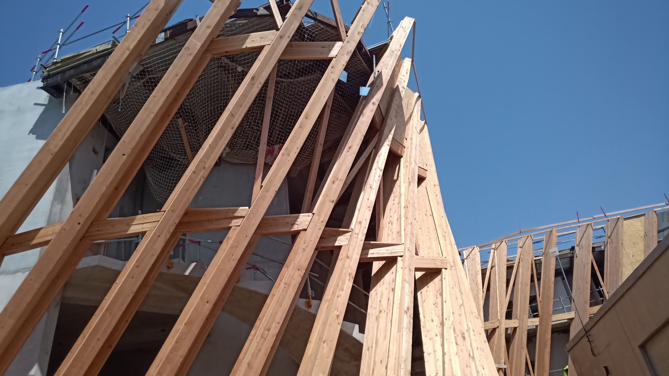 Ein Neubau im Rohbaustadium mit hölzernen Dachsparren und Fassadenelementen unter klarem Himmel.